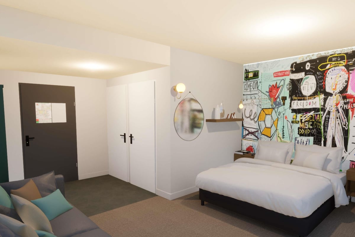A bedroom with a bed, a couch, a wardrobe, and a wall with graffiti art.