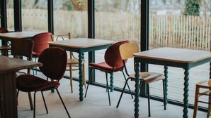 A restaurant interior with tables and chairs, large windows, and a view of a wooden fence and trees. - Greet Hotel Brest Aéroport (Guipavas)