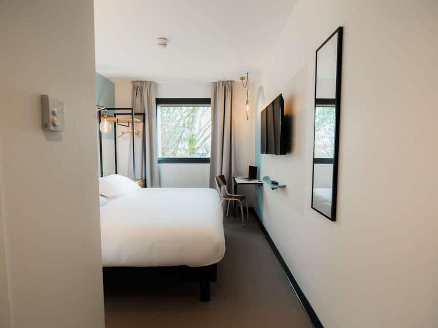 Una habitación de hotel con una cama, un escritorio, una silla, un televisor y una ventana.