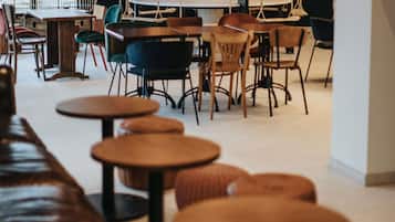 Interior de una cafetería con mesas y sillas redondas, un banco de madera y plantas colgantes.