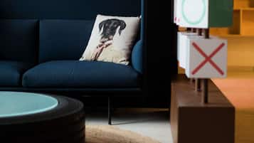Un sofá azul oscuro con un cojín decorativo, una mesa redonda y un bloque de madera con una 'X' roja.