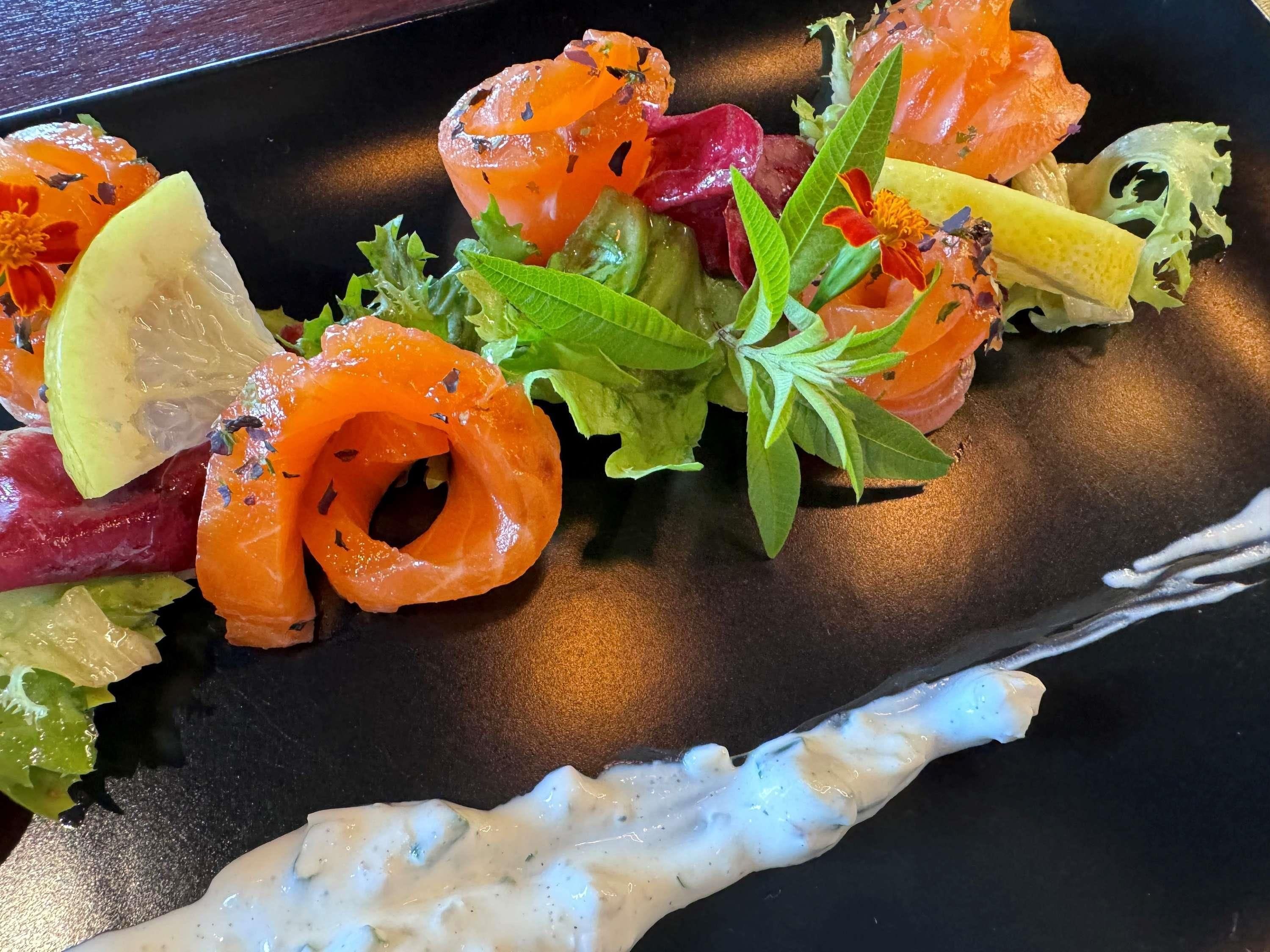 A plate of food with salmon, vegetables, and a creamy sauce.
