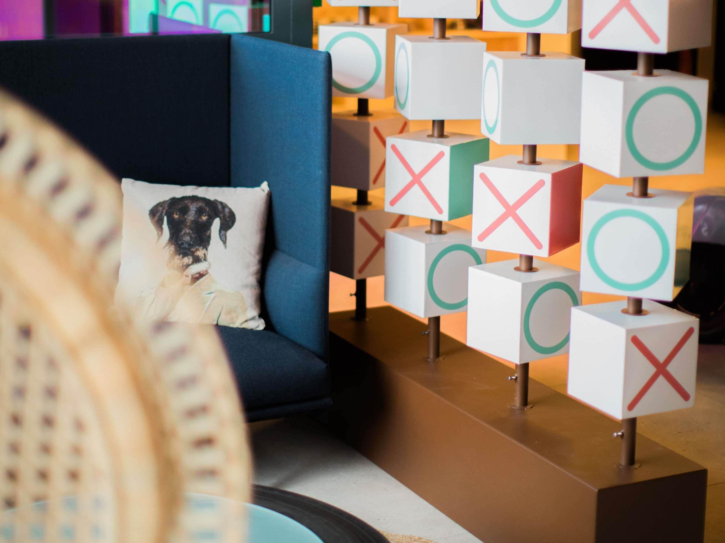 A modern hotel lobby with a blue sofa, a decorative pillow, and a wall of illuminated cubes.