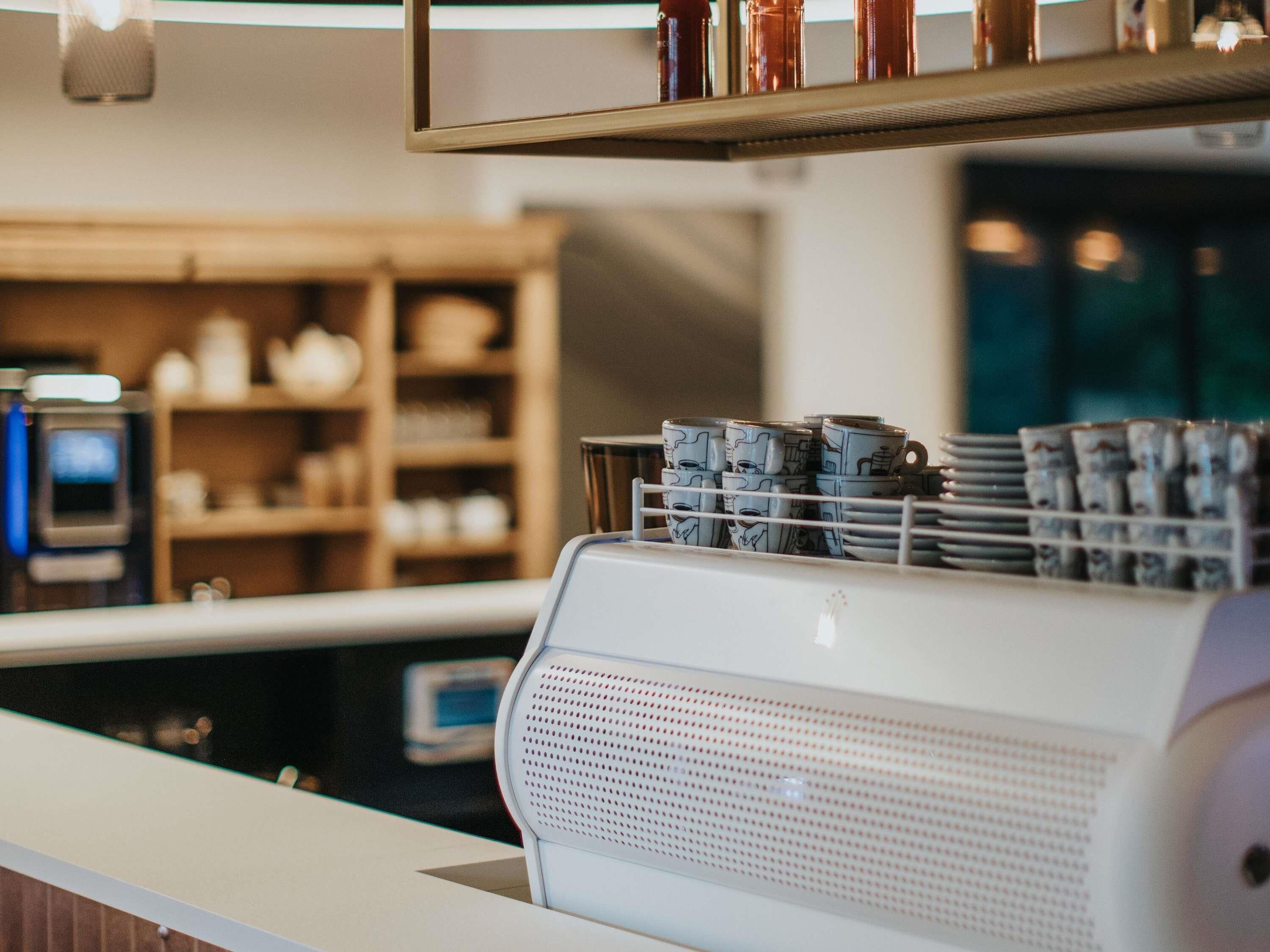 A coffee machine with a milk frother, a stack of blue cups, and a shelf with various items.