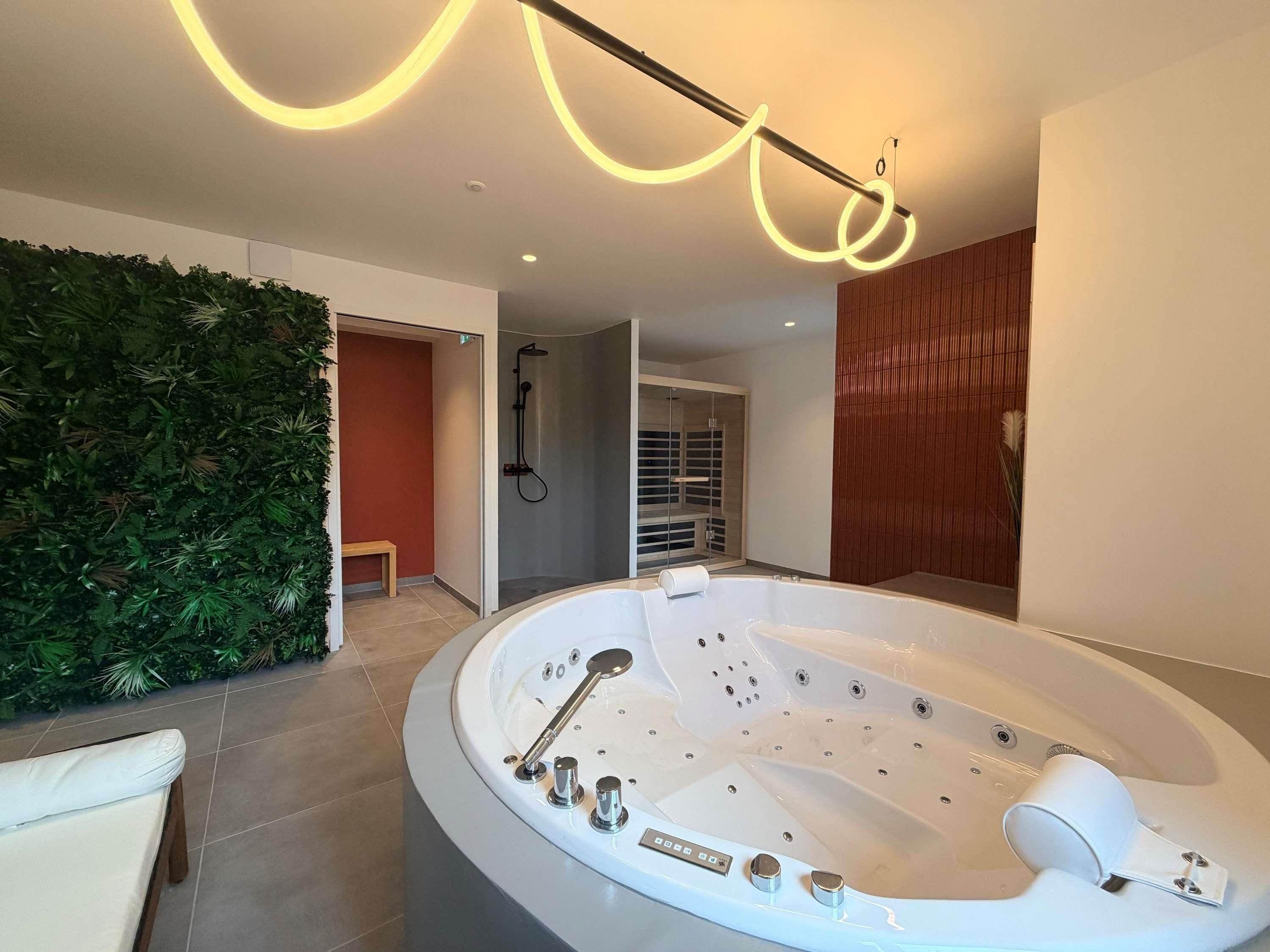 A modern bathroom with a freestanding bathtub, a shower area, and a green wall with plants.