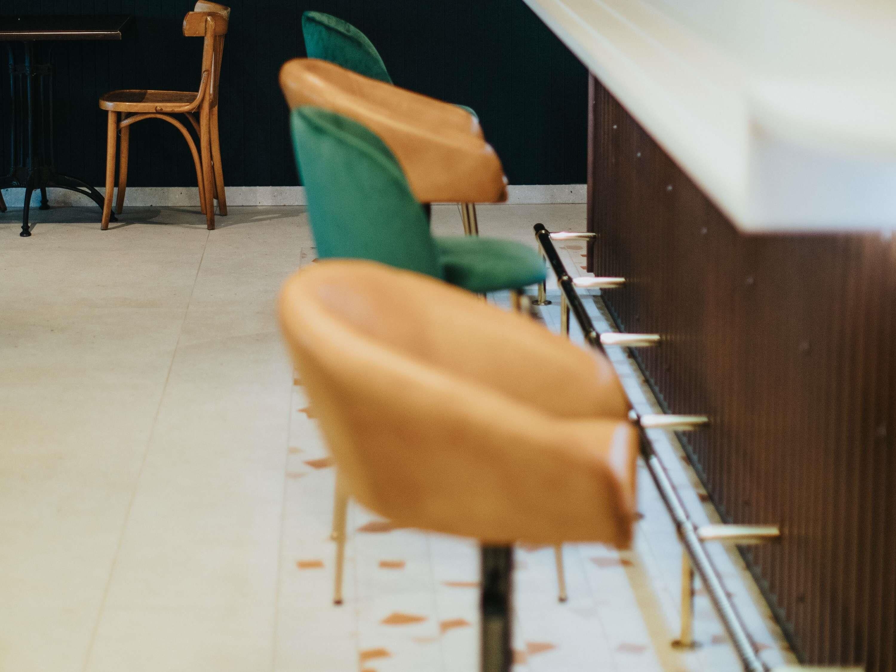 Une rangée de chaises avec des pieds en métal et une table en bois, dans une pièce dont le sol est recouvert de carreaux.