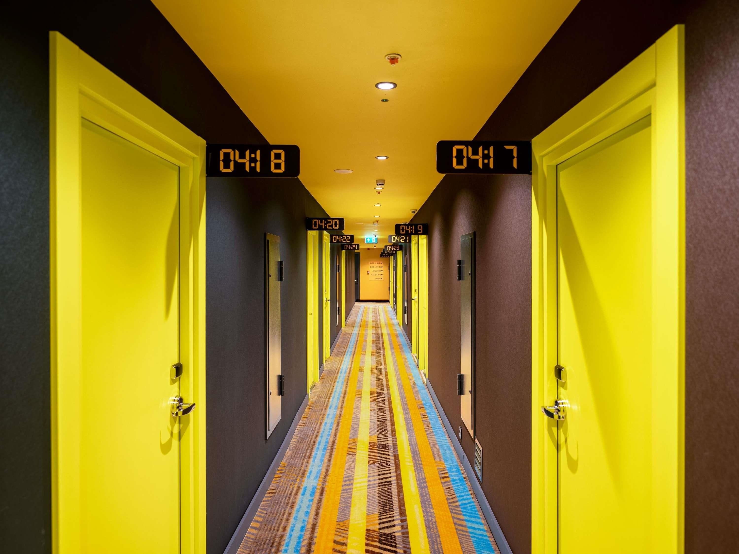 A hotel hallway with doors numbered from 04:08 to 04:23, leading to a carpeted area.