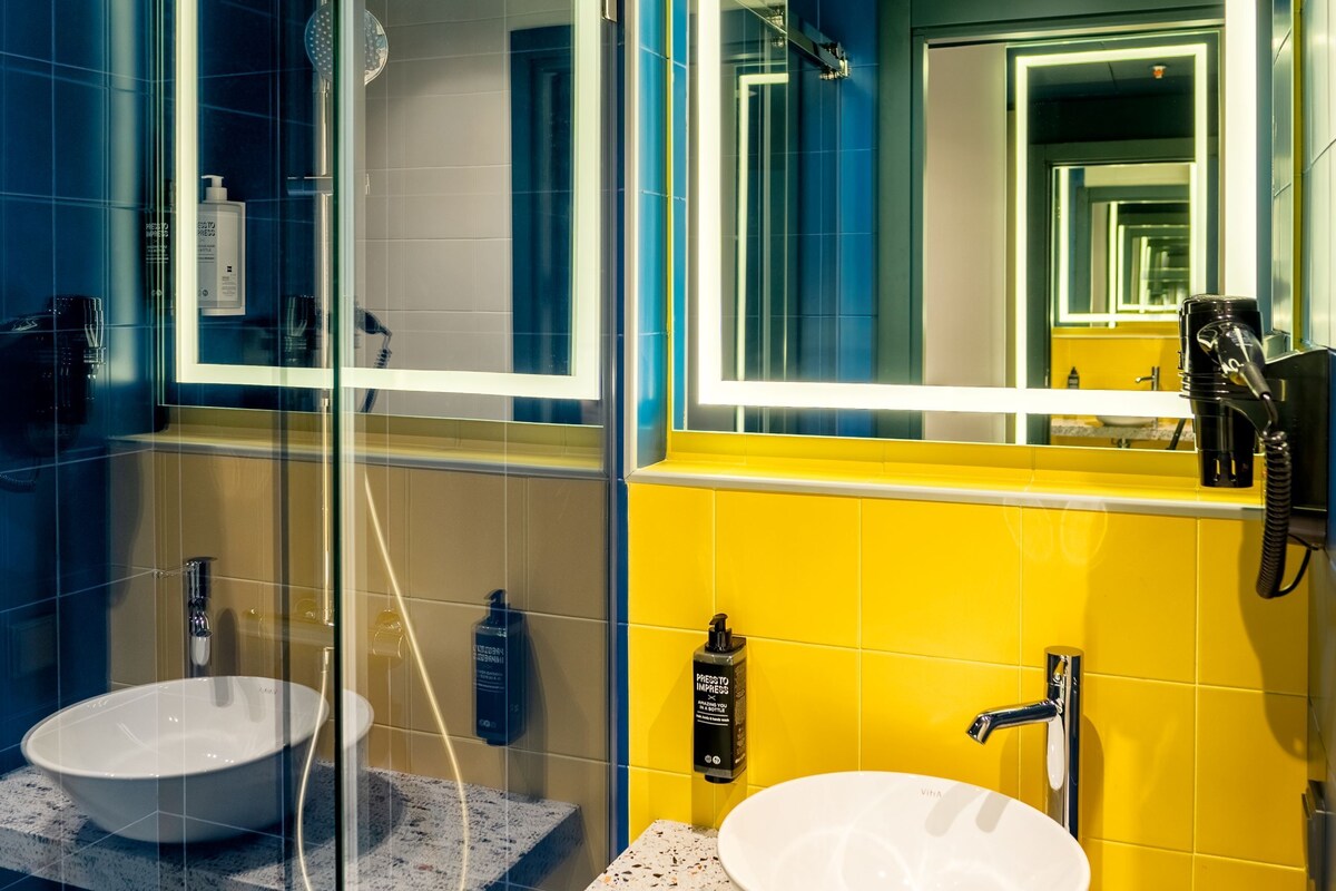 A modern bathroom with a glass-enclosed shower, a white sink, and a yellow-tiled wall.