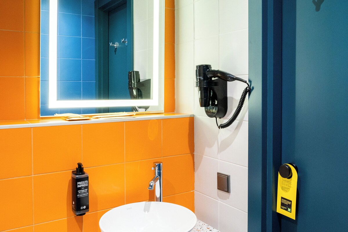 A bathroom with a white sink, a mirror with illuminated frame, a hairdryer, and a blue door.