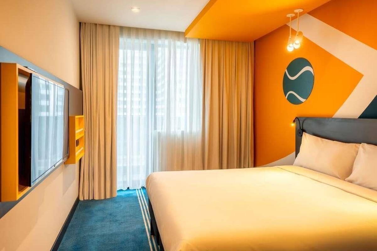 A hotel room with a bed, curtains, a TV, and a wall-mounted light fixture.