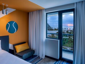 A hotel room with a bed, a sofa, a large window with curtains, a wall-mounted light fixture, and a circular artwork. - ibis Styles Batumi  (Batumi)