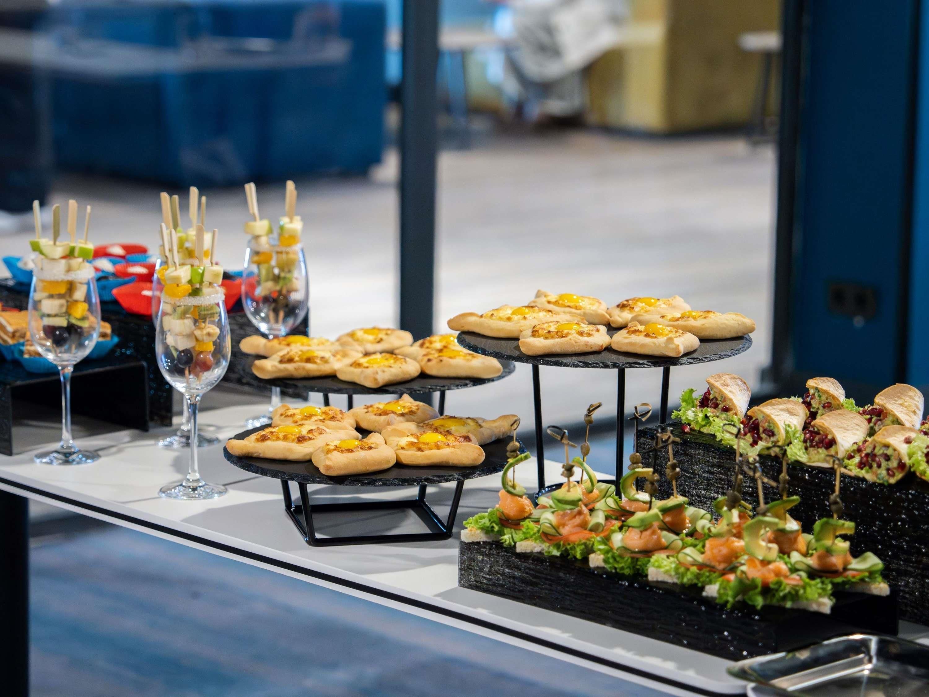 En buffet med forskellige retter, herunder forretter og desserter, anrettet på sorte stativer.