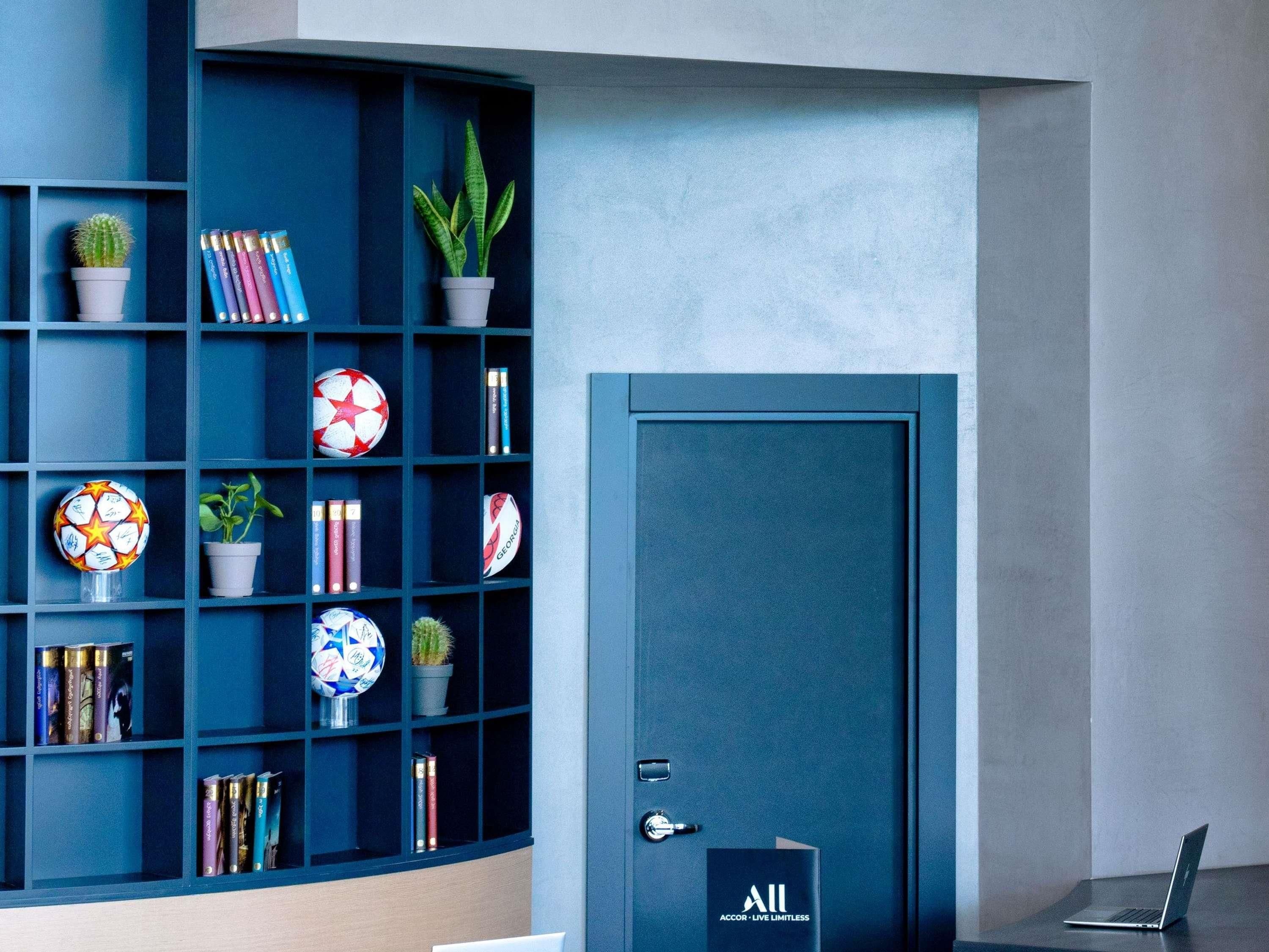 A modern room with a dark blue bookshelf containing books, a soccer ball, and a potted plant. A closed door with a lock is visible to the right.