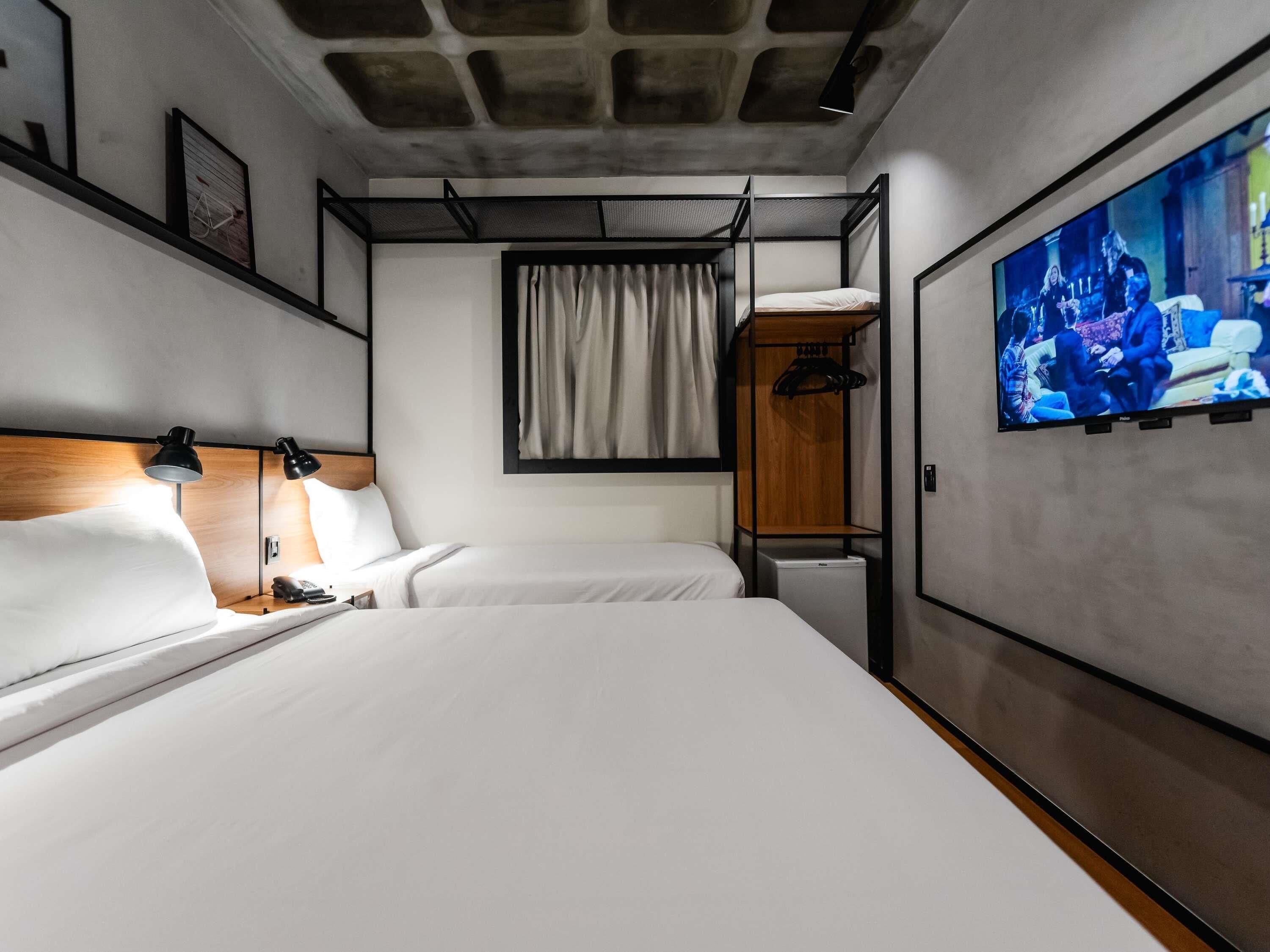 A hotel room with a bunk bed, a desk with a lamp, a TV, and a wardrobe.