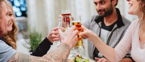 A group of people toasting with beer glasses at a dining table with food and a bowl of salad.