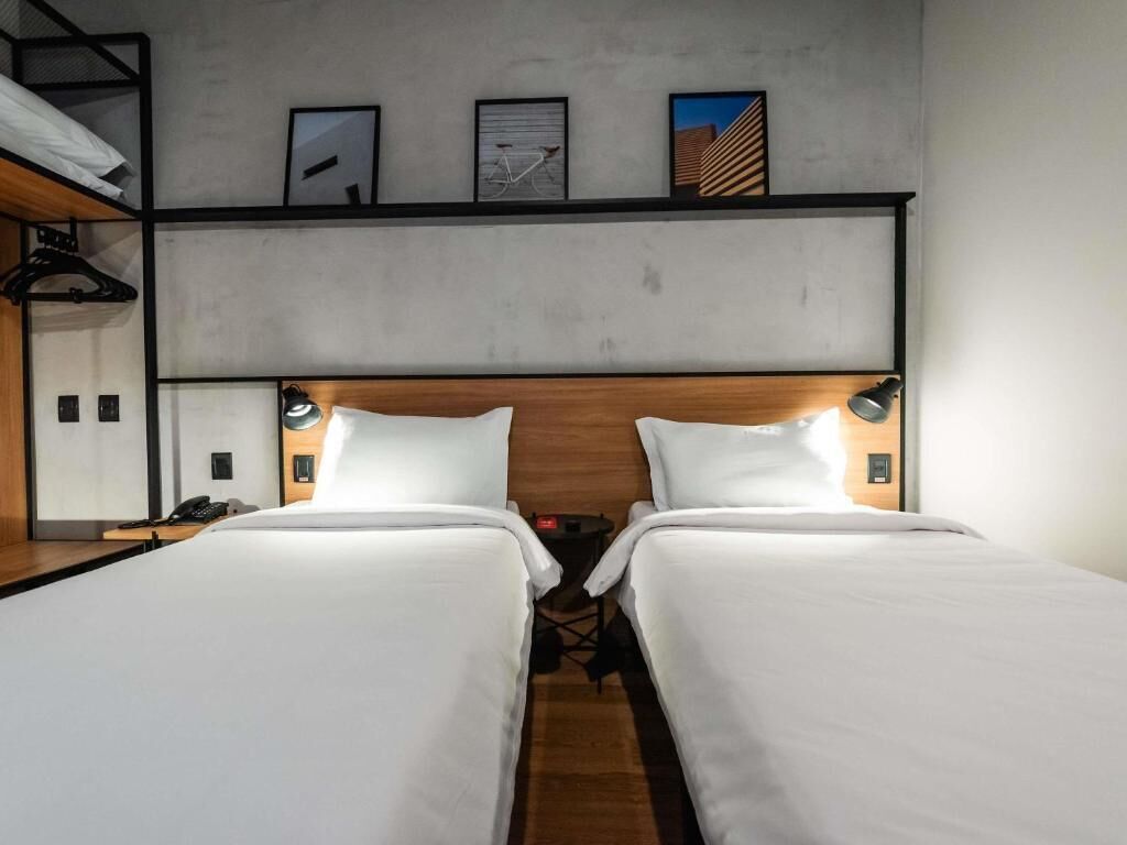 A hotel room with two single beds, a wooden headboard, bedside lamps, a small table, and a mirror.