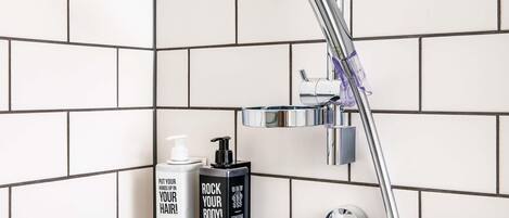 A shower area with a handheld showerhead, a soap dispenser, and a body wash bottle.