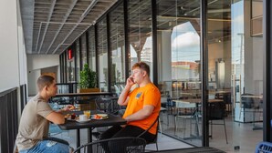 Un café en plein air avec des tables et des chaises, de grandes fenêtres et une vue sur le paysage urbain.