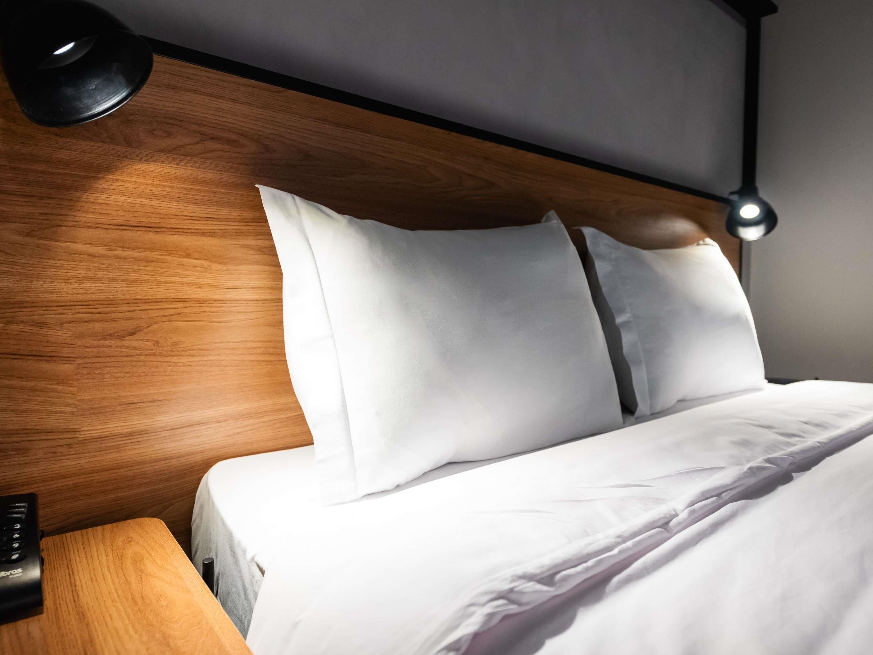 A neatly made bed with white linens, a wooden headboard, and a bedside table with a lamp.
