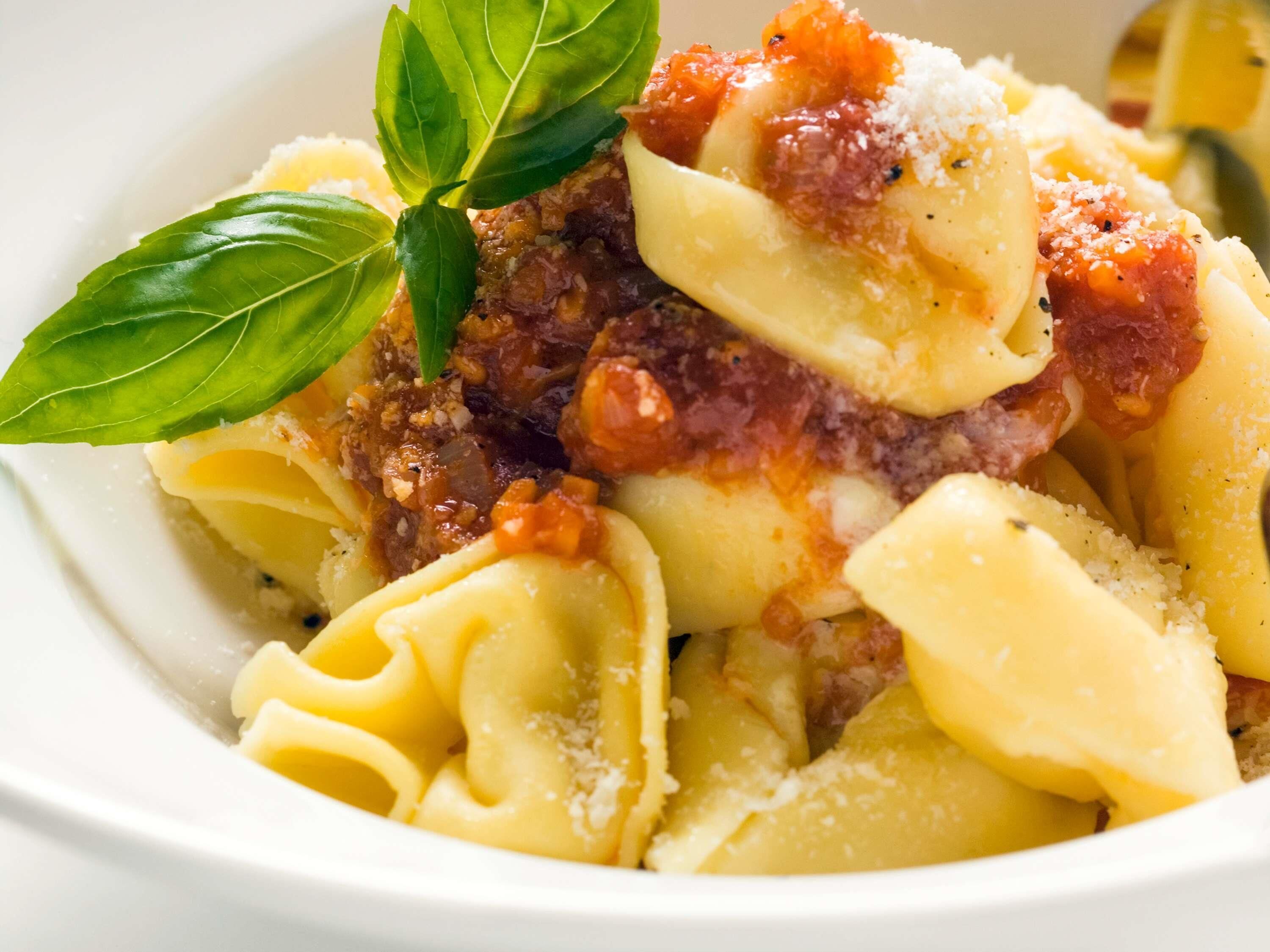 Un plato de pasta con salsa de tomate, adornado con albahaca y queso rallado.