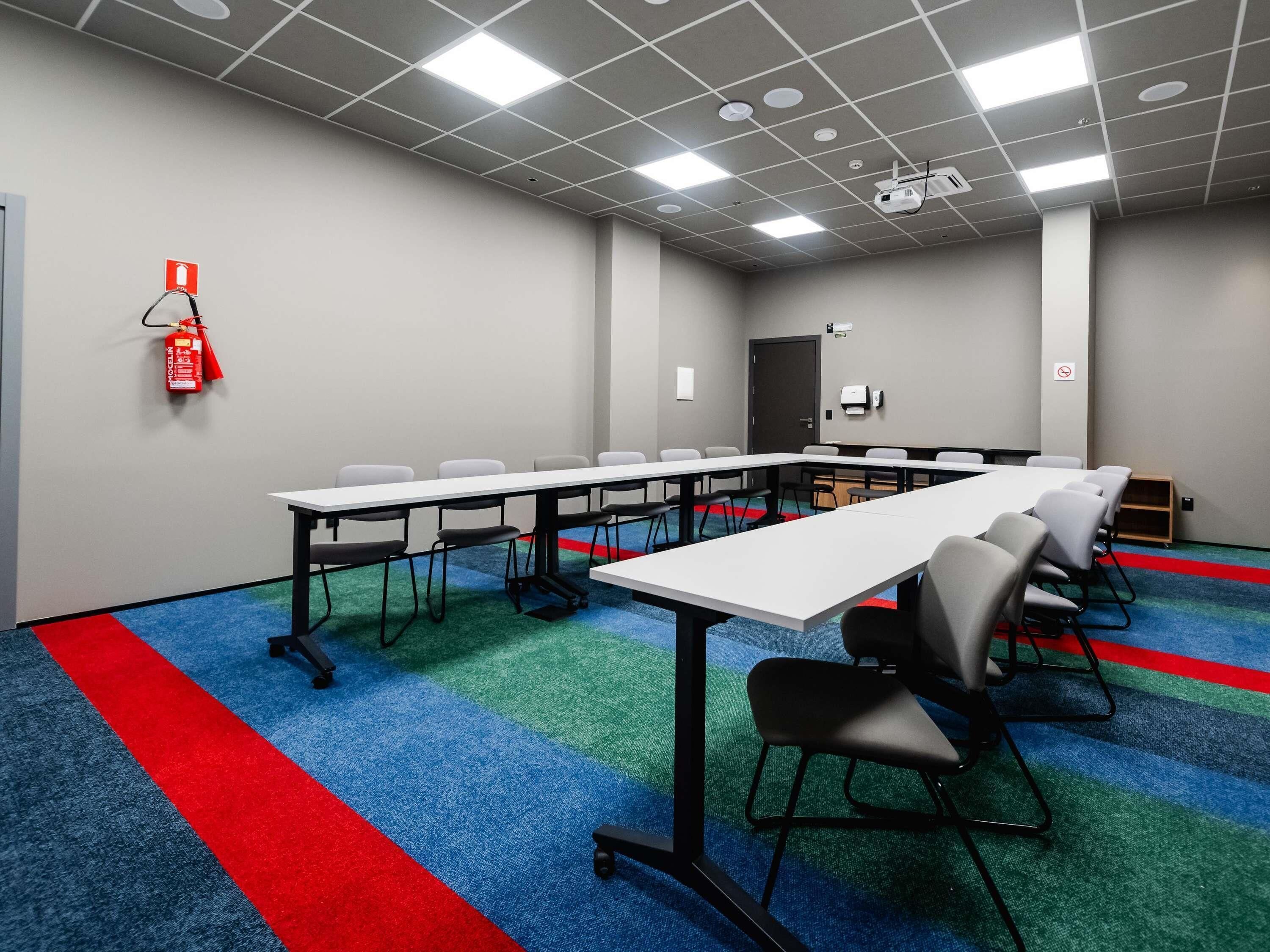 A conference room with a long table, chairs, a fire extinguisher, and a projector.