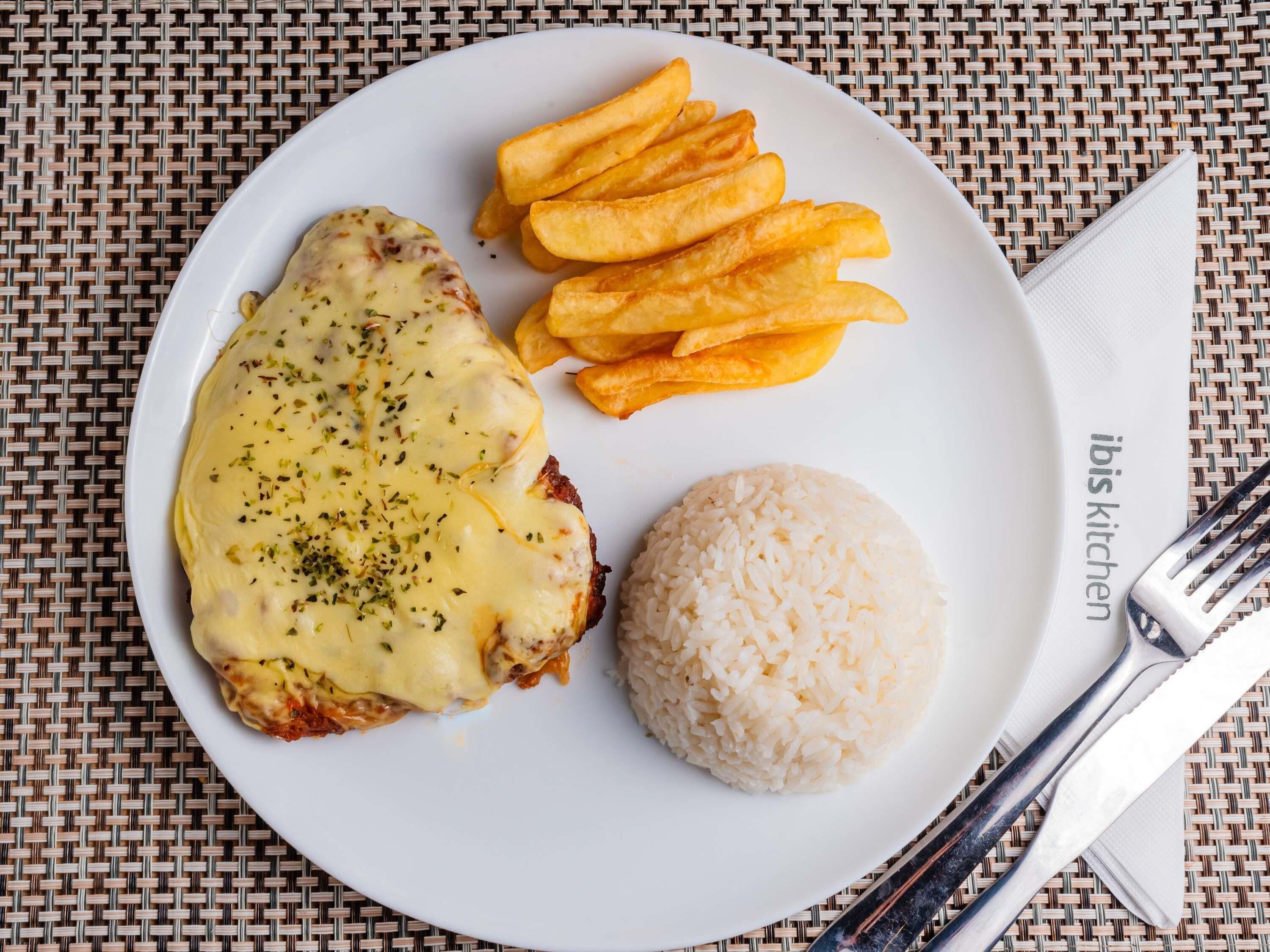 A plate with a meat dish, fries, and rice on a woven mat.