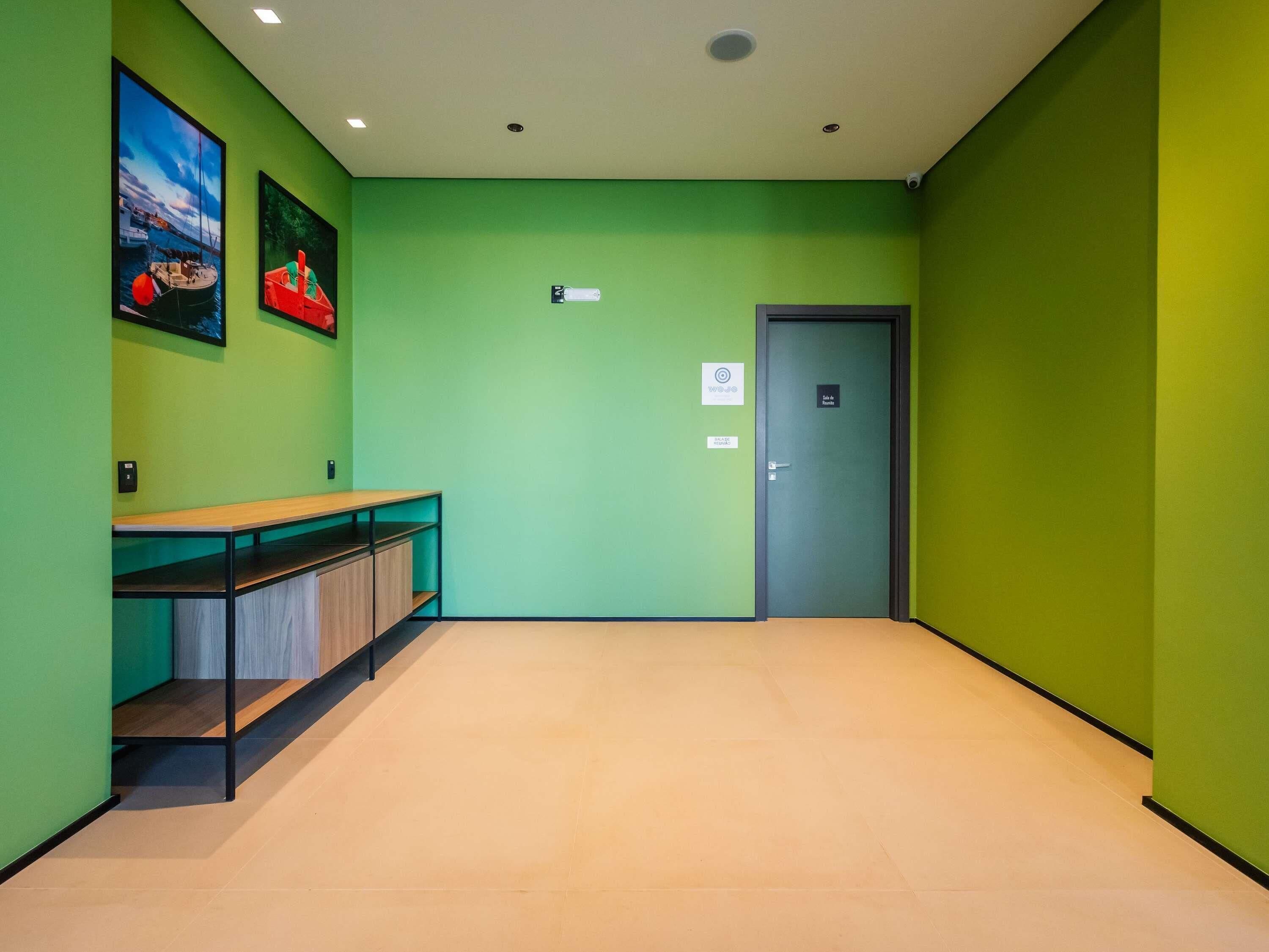 Un pasillo con paredes verdes, un banco de madera, una puerta con la etiqueta 'Lobby' y un cartel que indica un servicio 'W.O.J.O'.