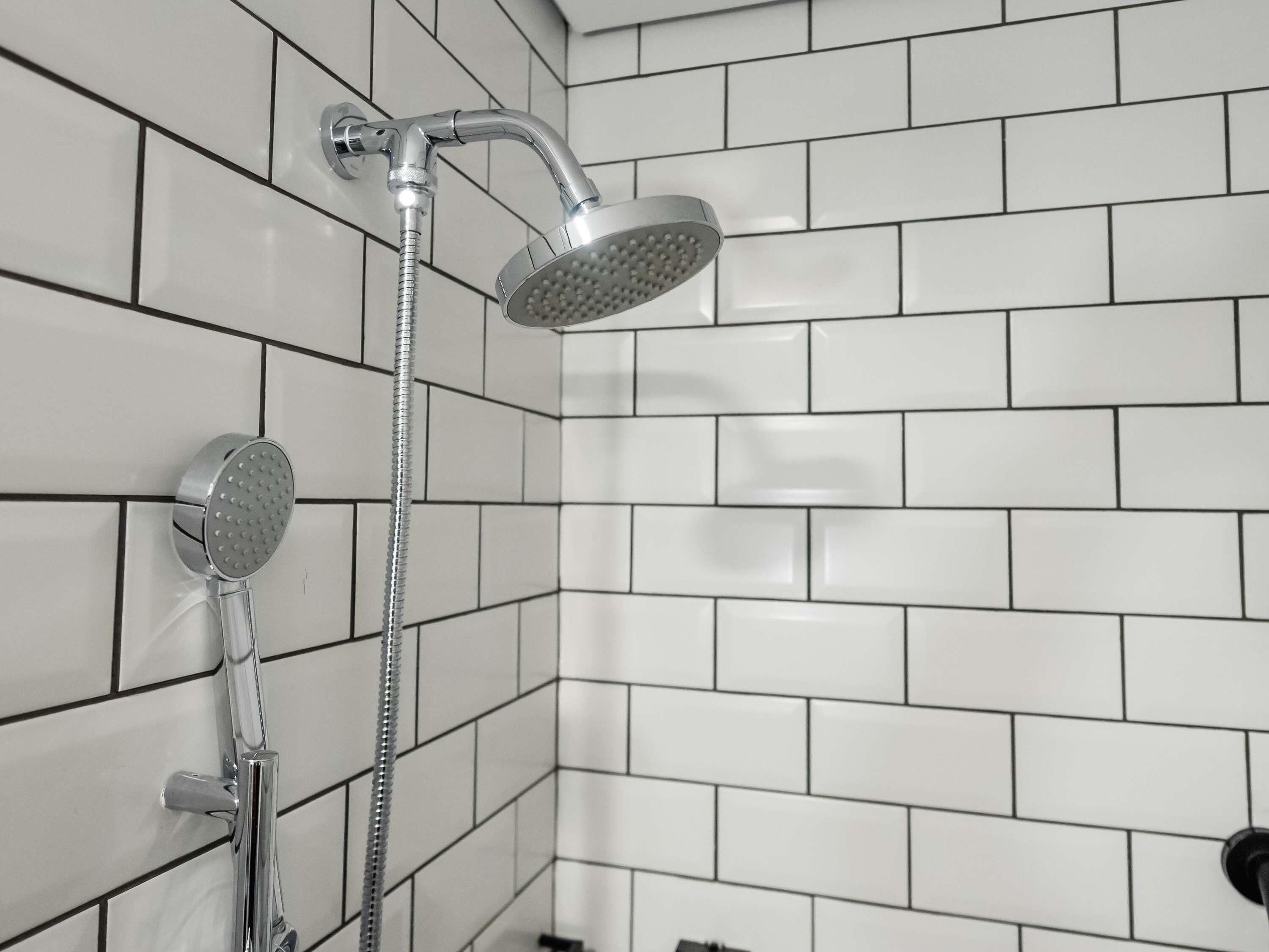 Een badkamer met witte betegelde wanden en een douche met een handdouche en een vaste douchekop.
