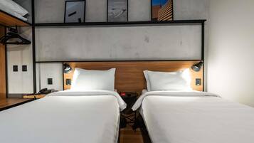 A hotel room with two beds, a wooden headboard, bedside lamps, a phone, and a shelf with a bicycle.
