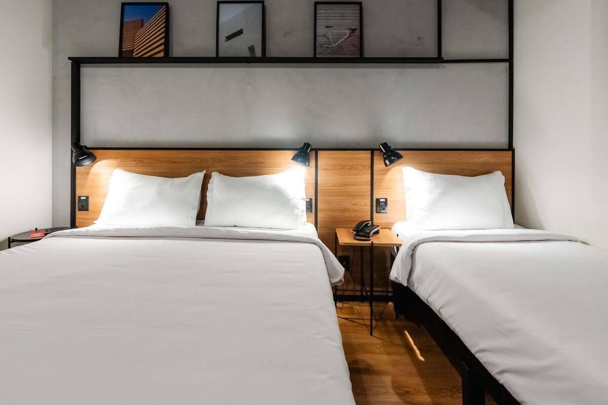 A hotel room with two beds, wooden headboards, and bedside tables with lamps.
