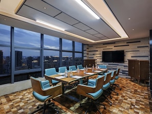 A conference room with a city view, large windows, a flat-screen TV, and a checkered floor.