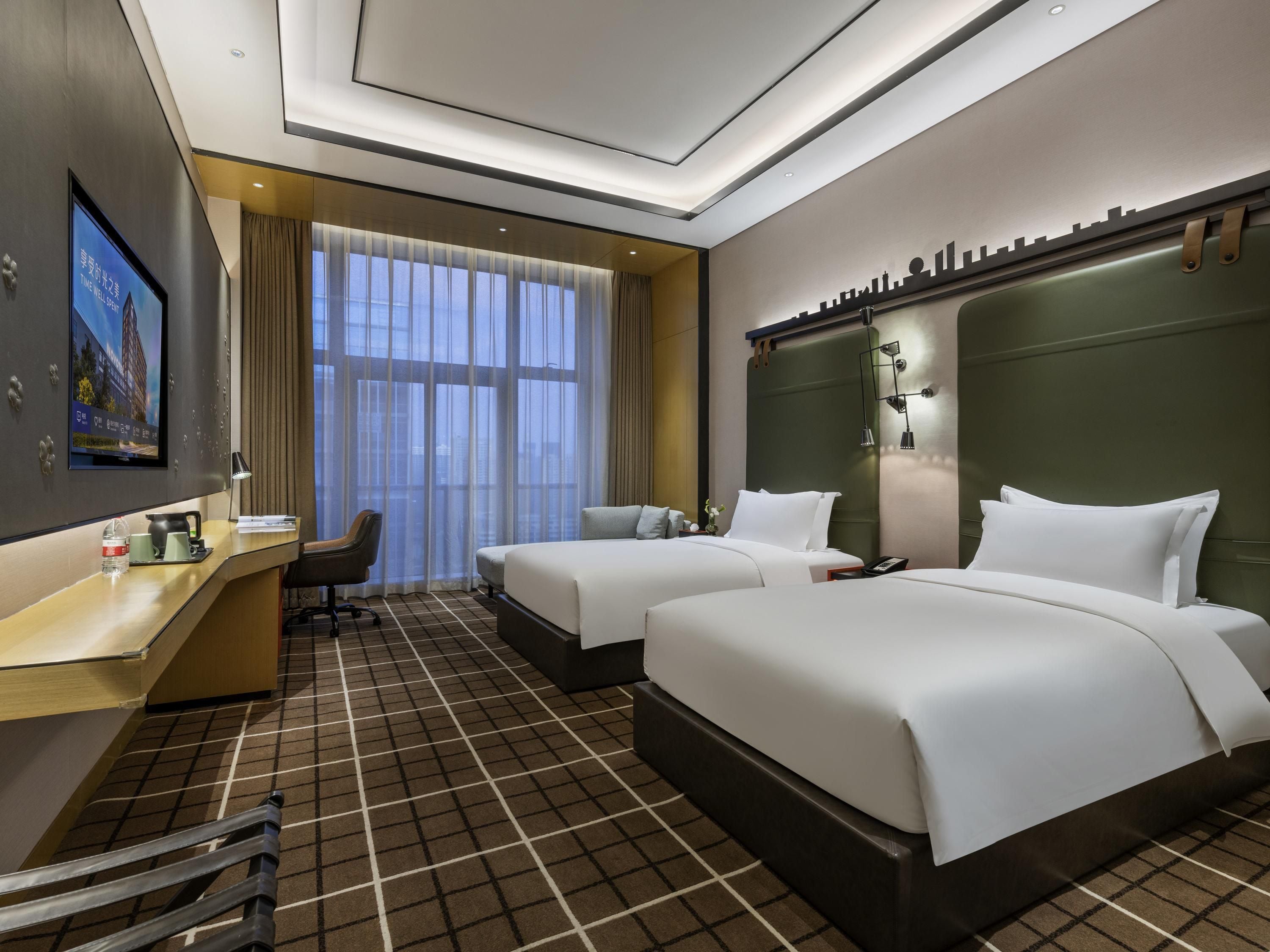 A hotel room with two beds, a desk, a chair, and a television.