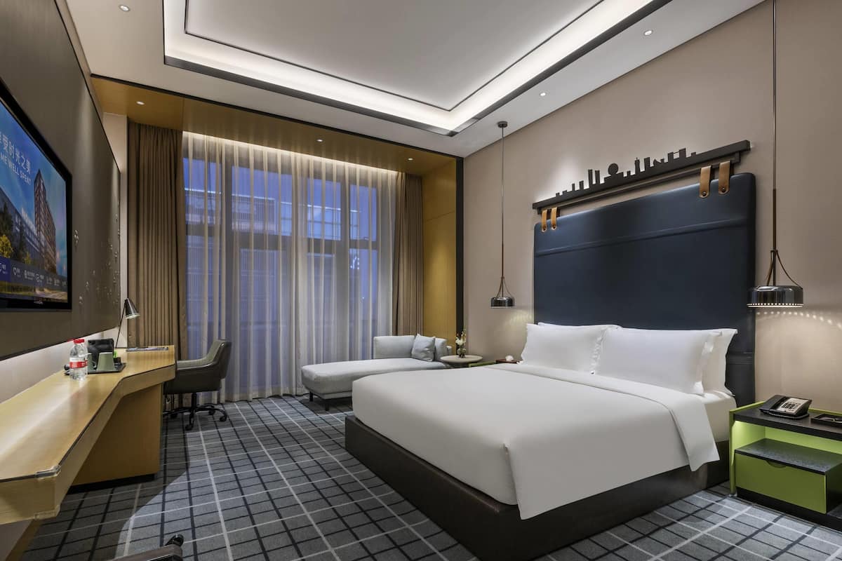 Una habitación de hotel moderna con una cama grande, un escritorio, una silla y un televisor.