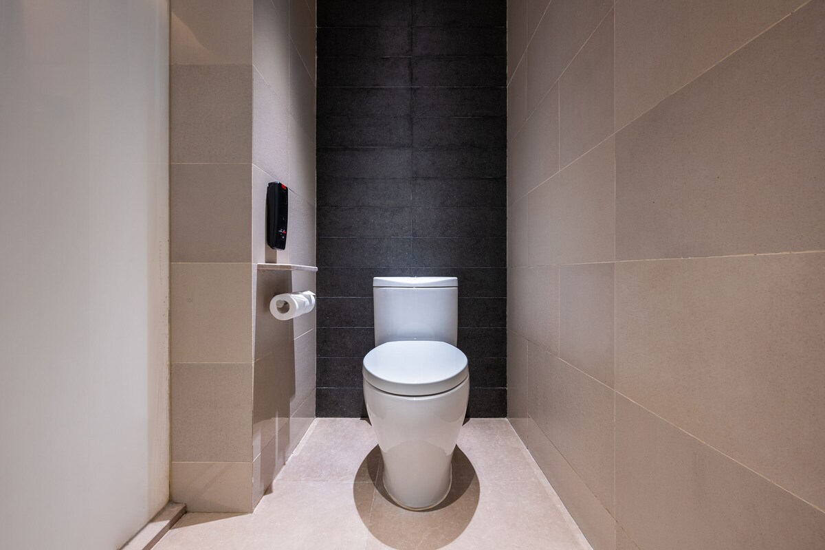 A modern bathroom with a white toilet, dark tiled walls, and a beige floor.