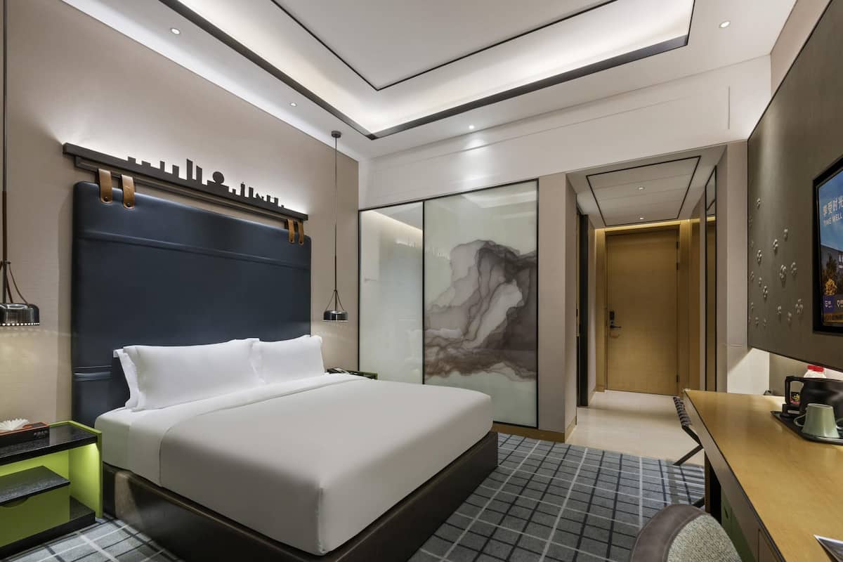 Una habitación de hotel moderna con una cama grande, un escritorio y un baño con cabina de ducha de vidrio.