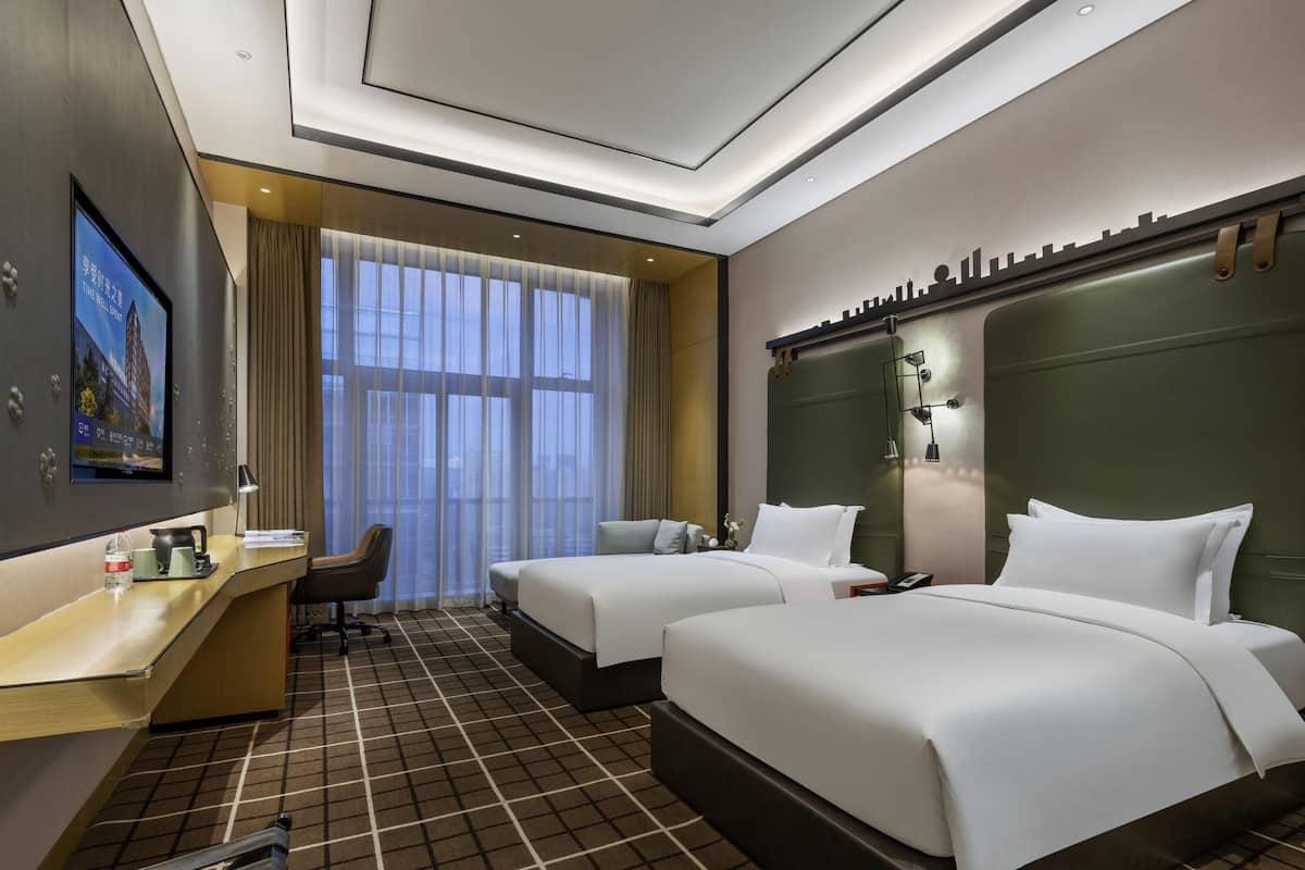 Habitación de hotel con dos camas, un escritorio, una silla y un televisor.