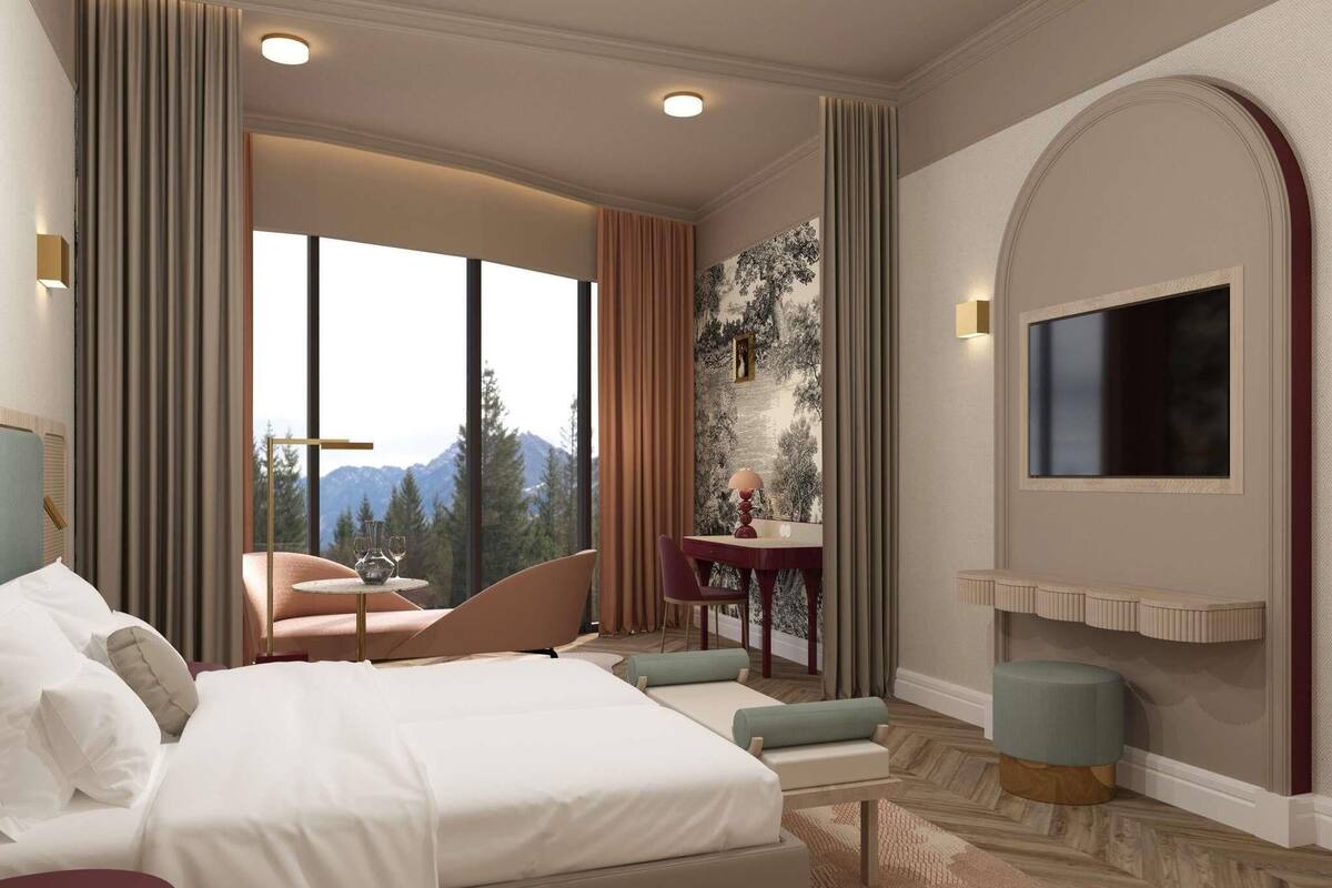A hotel room with a large bed, a seating area with a table, a TV mounted on the wall, and a view of mountains through the window.