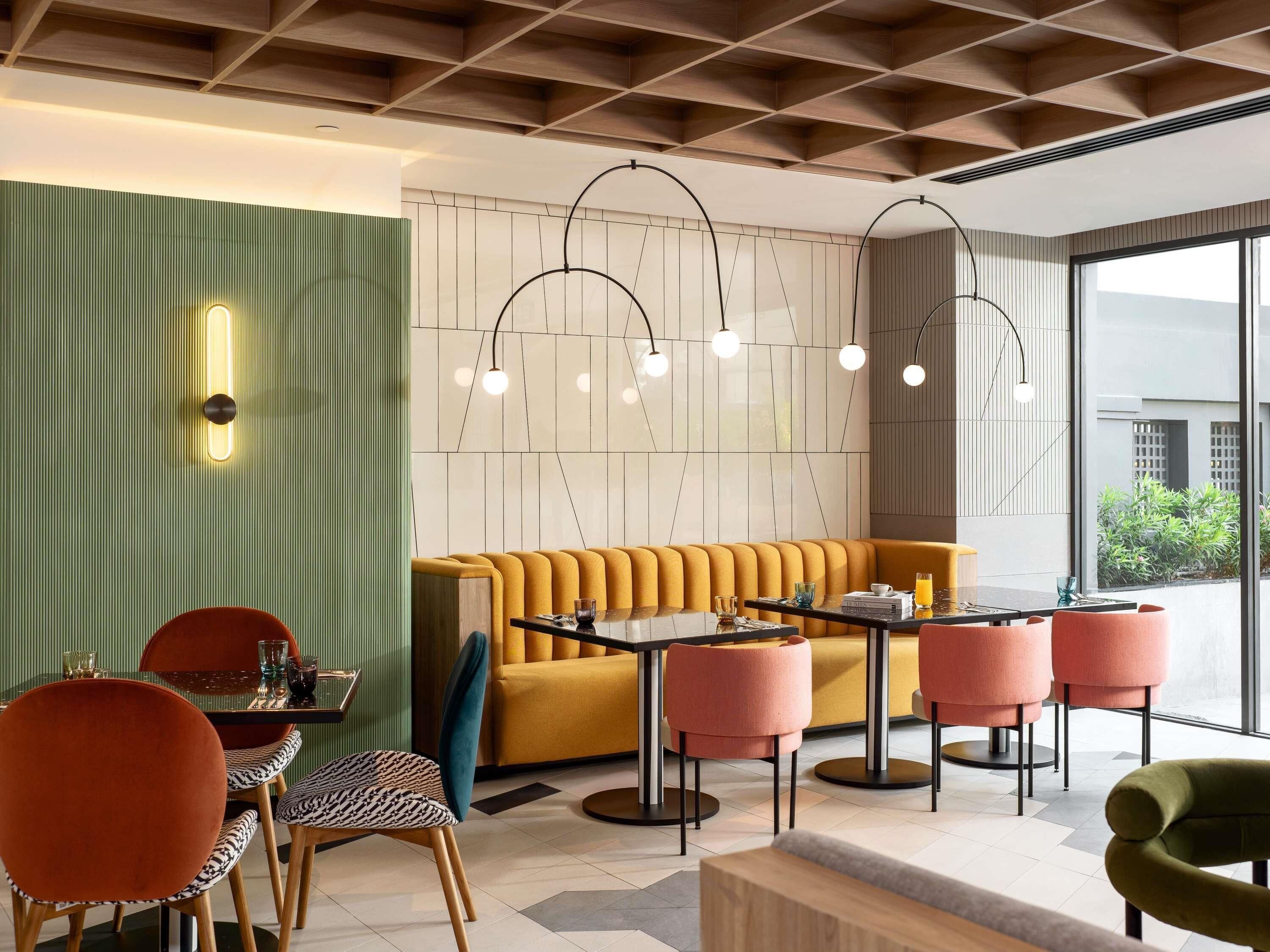 A modern interior with a green accent wall, a yellow sofa, and a dining area with pink chairs.