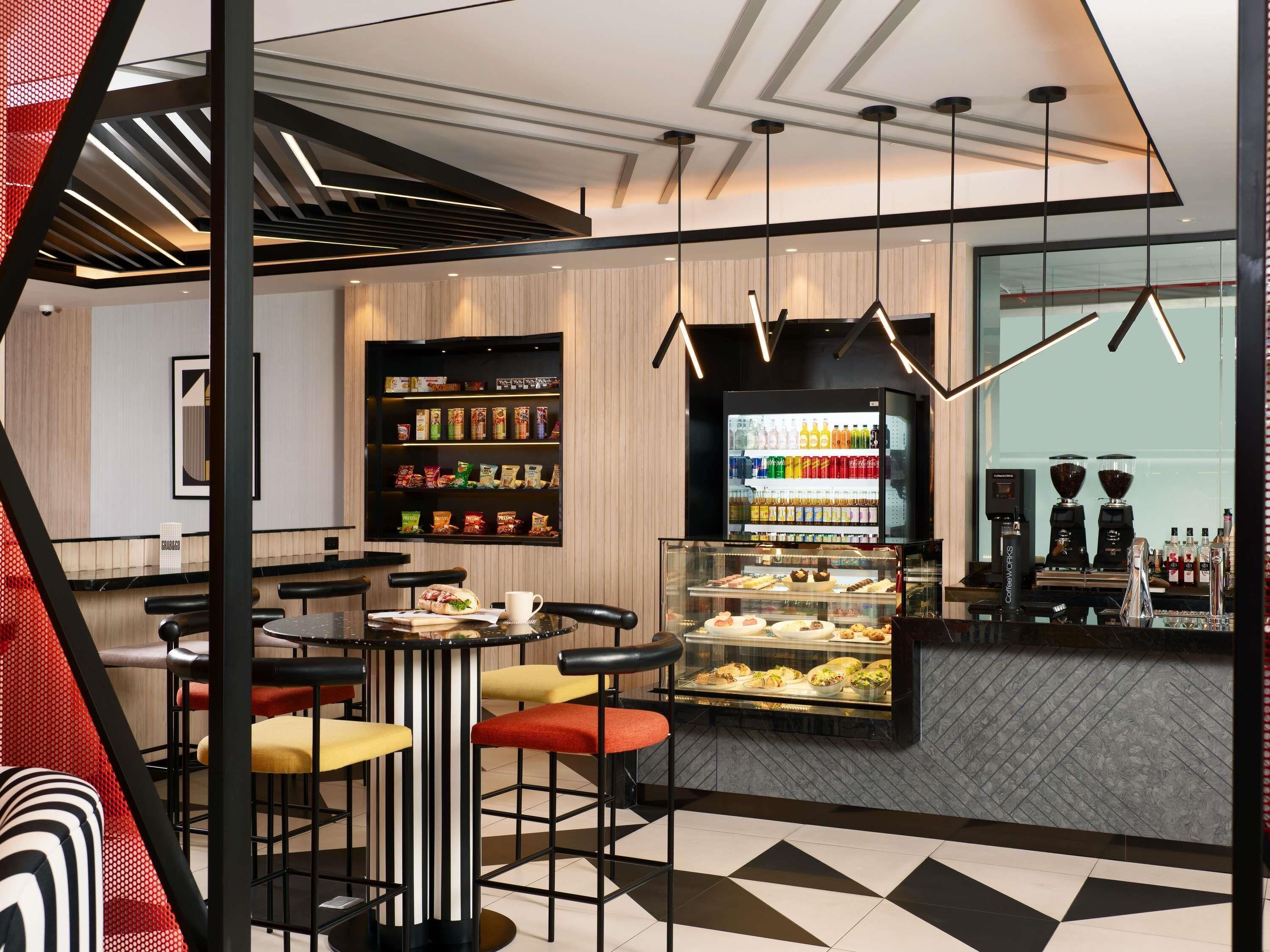 A modern cafe interior with a bar area, seating, a display case with pastries, and a beverage refrigerator.