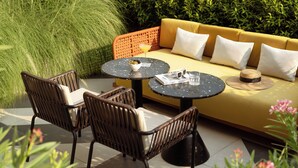 A sunlit outdoor seating area with wicker chairs, a round table, and a sofa with cushions. - TRIBE Living Bangkok Sukhumvit 39 by AccorHotels (Bangkok)