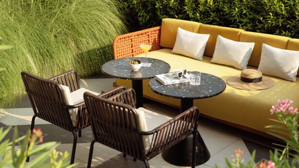 A sunlit outdoor seating area with wicker chairs, a round table, and a sofa with cushions. - TRIBE Living Bangkok Sukhumvit 39 by AccorHotels (Bangkok)