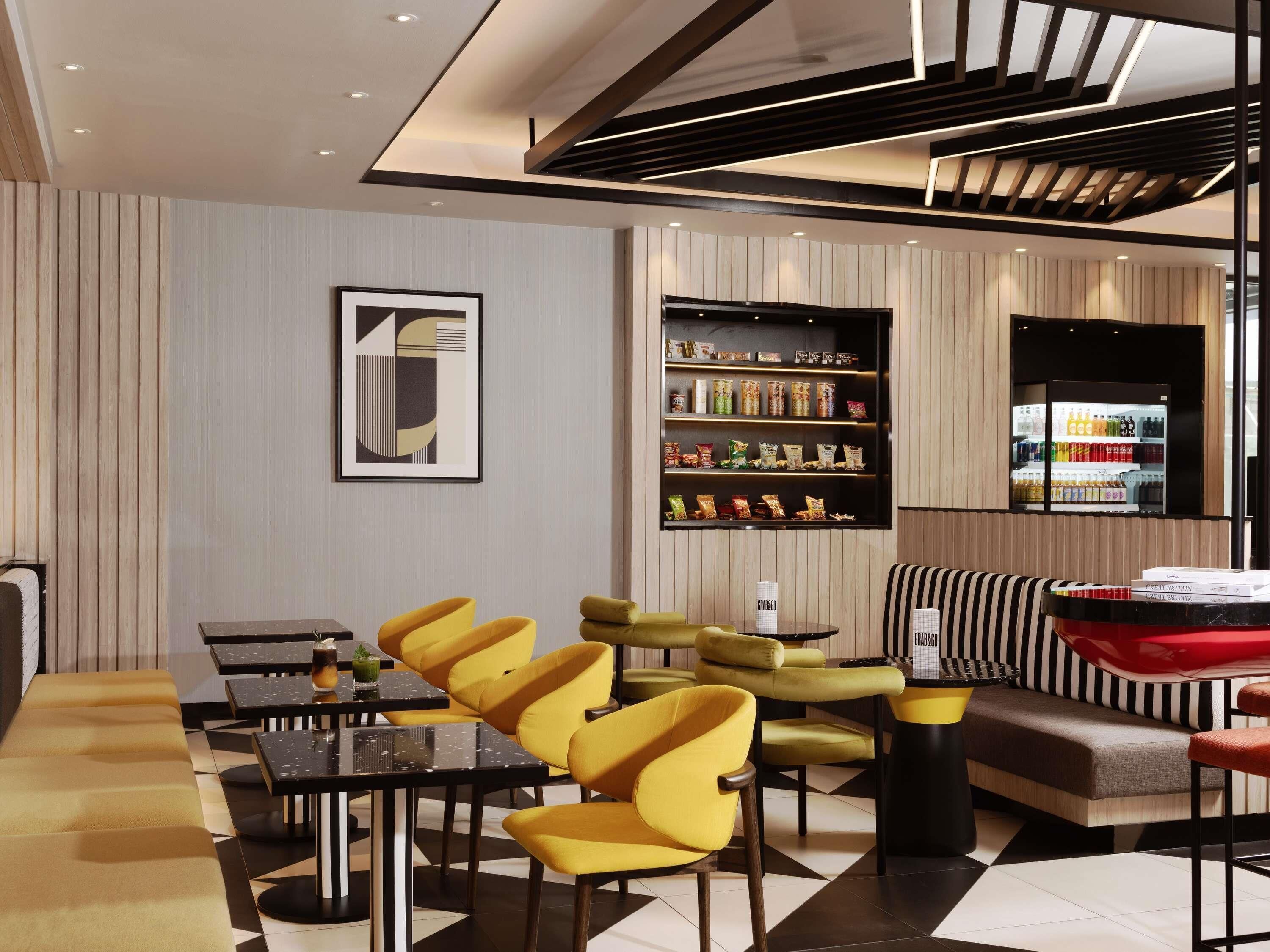 A modern interior with a dining area, yellow chairs, a black and white sofa, and a wall-mounted shelf with snacks.