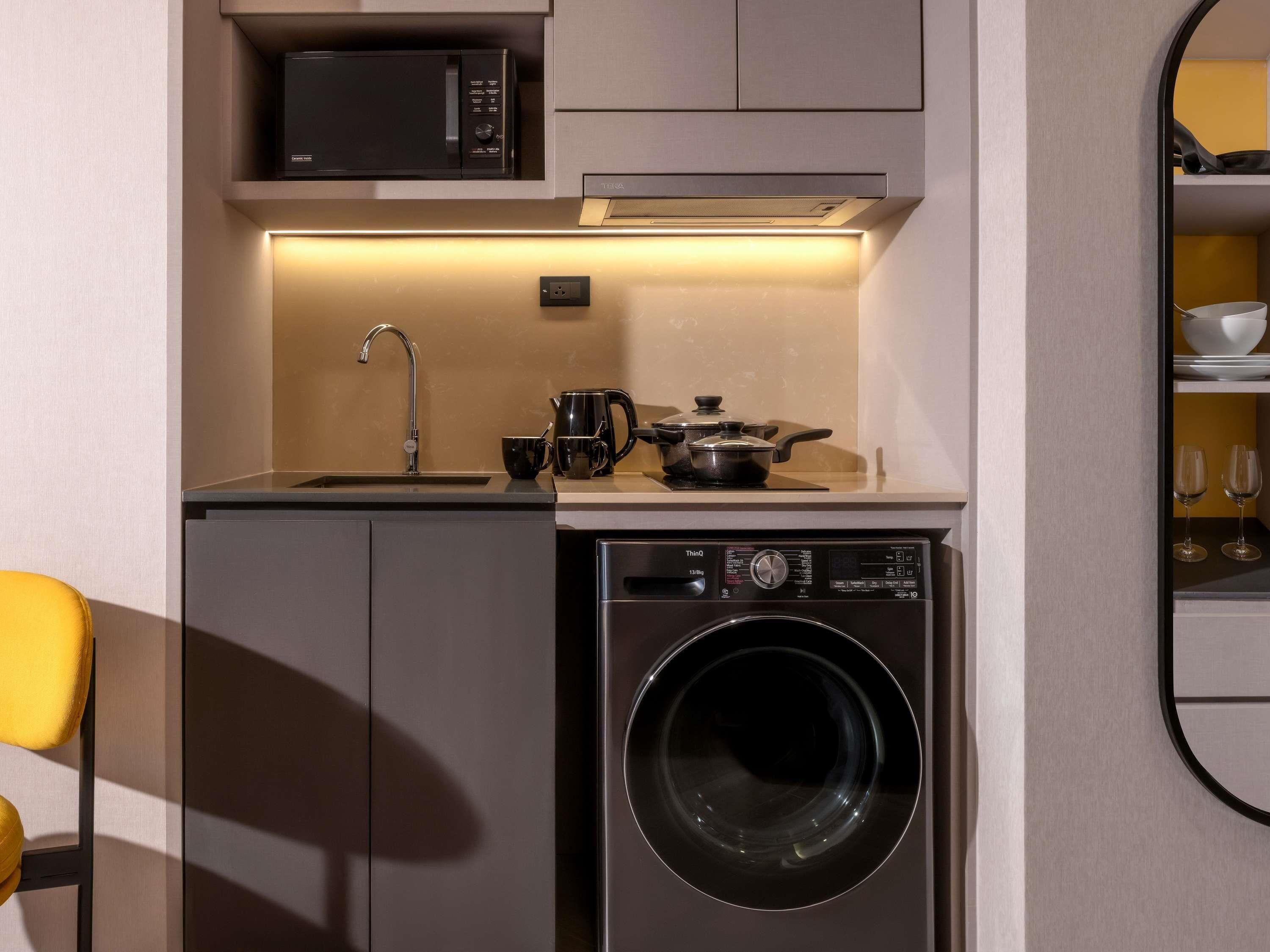 Une cuisine compacte équipée d’un four à micro-ondes, d’un évier, d’une bouilloire et d’un lave-linge encastré.
