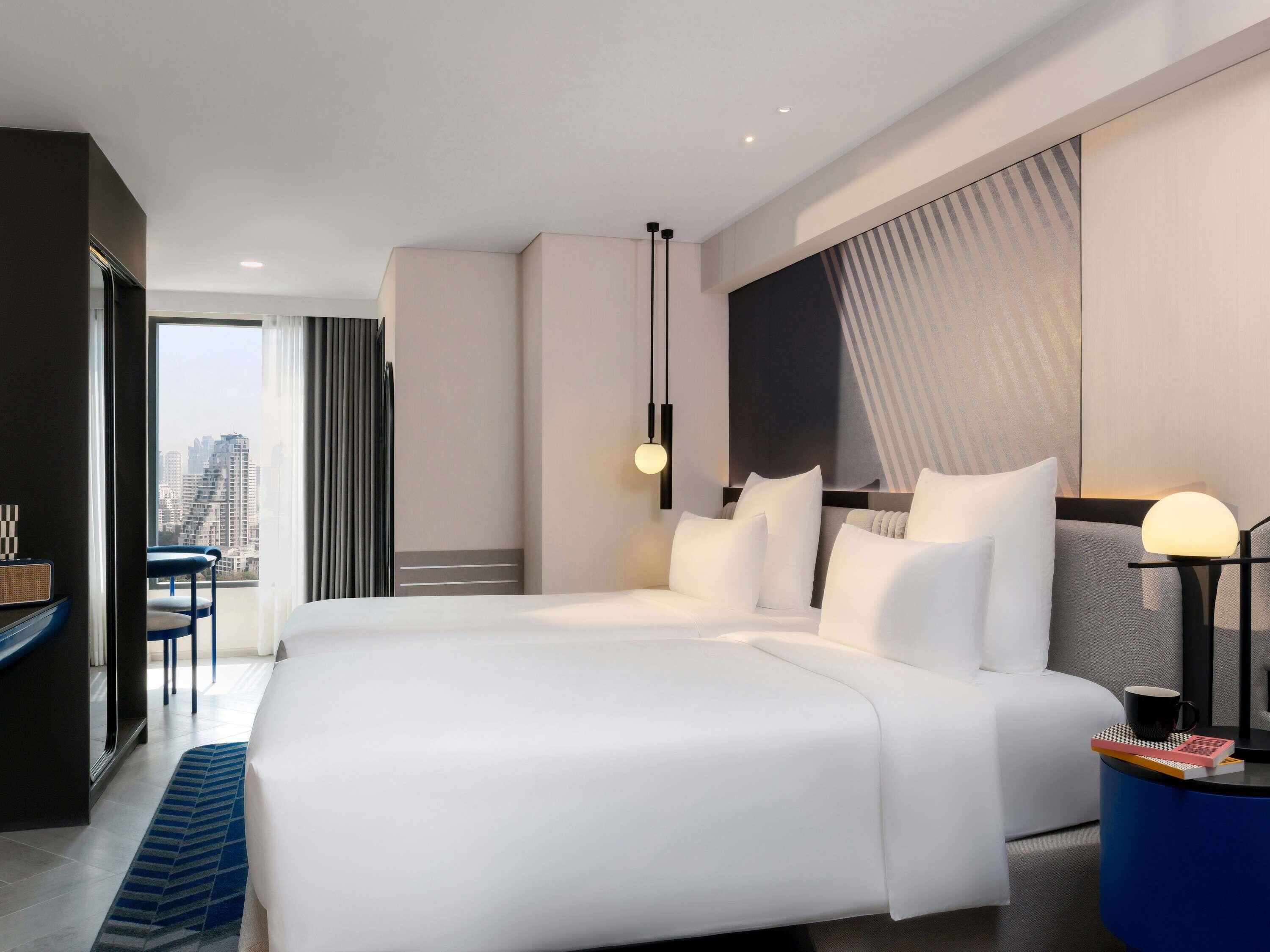 A modern hotel room with a large bed, a desk, and a view of the cityscape.