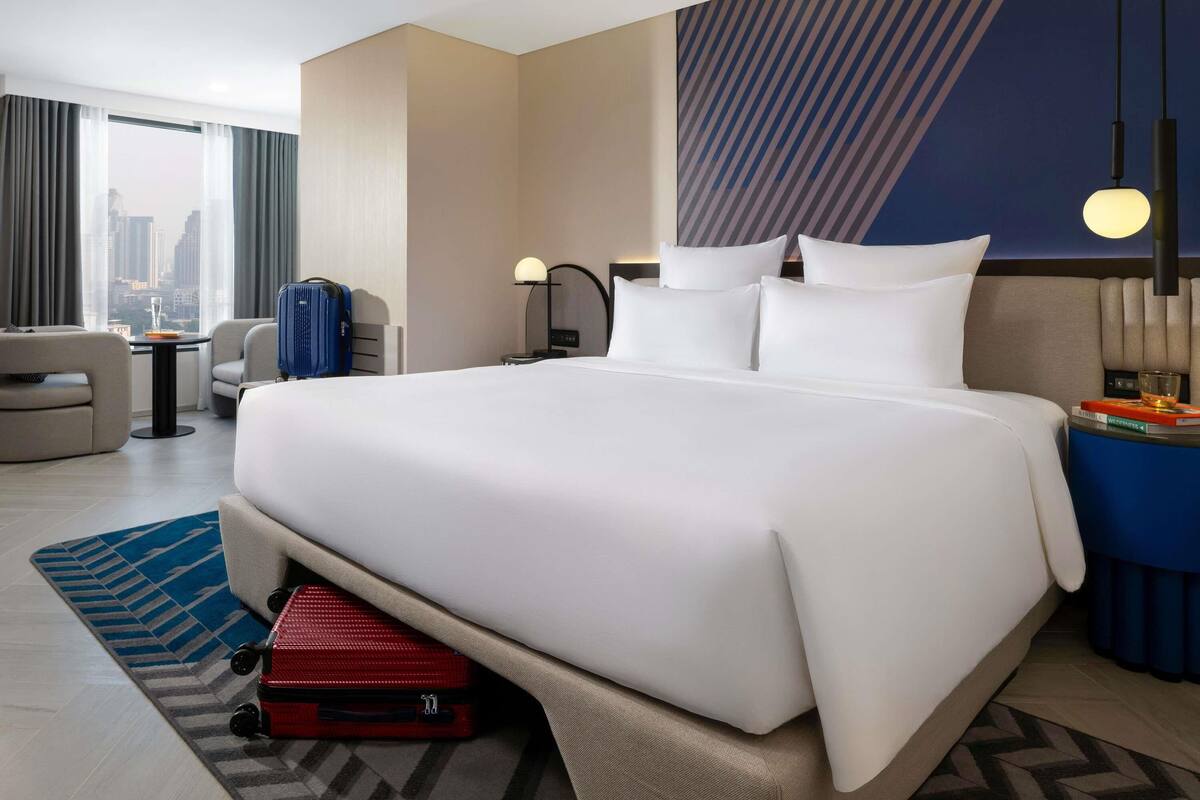 Habitación de hotel con una cama grande, un escritorio, una silla, una maleta y vistas a la ciudad.
