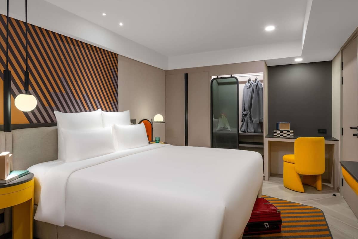 Una habitación de hotel moderna con una cama grande, un escritorio, una silla, un armario y un espejo.