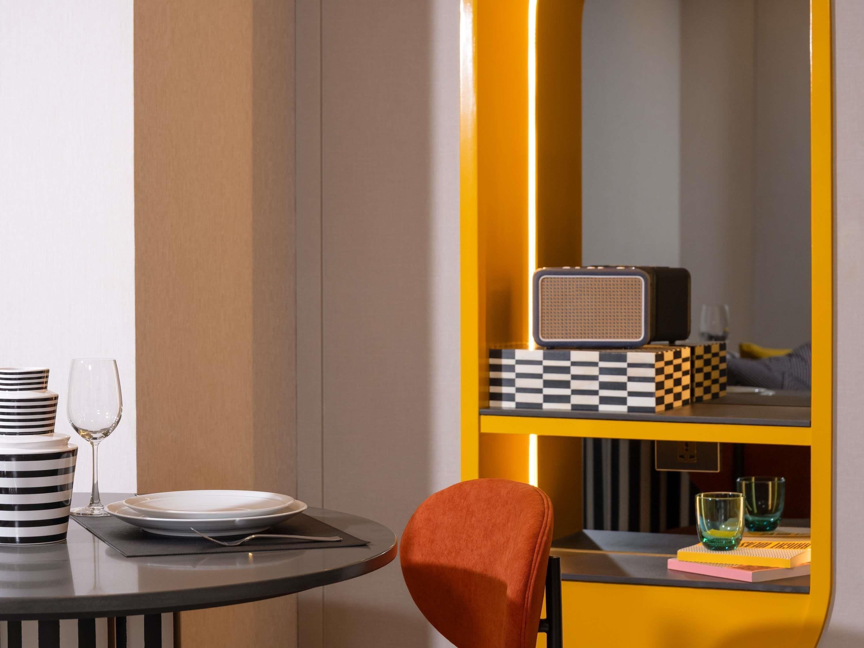 A dining area with a table set for two, a chair, a radio, and a checkered shelf with glasses.