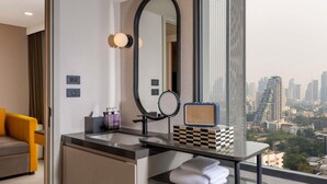 A modern bathroom with a large mirror, a small speaker, and a glass shelf with towels.