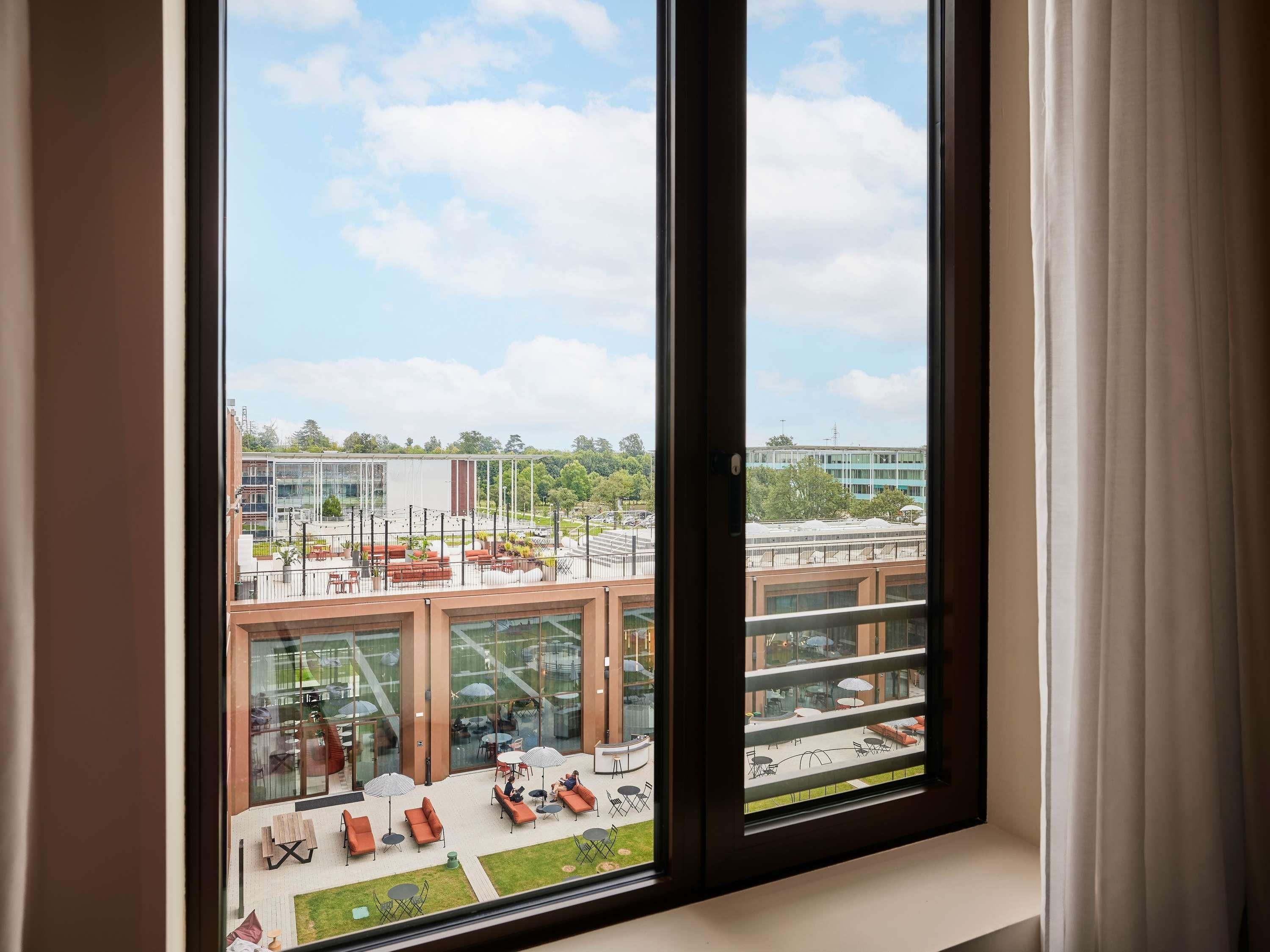 A modern building with large windows, outdoor seating, and a view of a parking area.