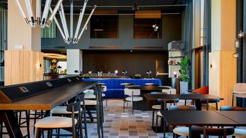 Un bar moderno con una barra larga, diversas opciones de asientos que incluyen taburetes y mesas, y una combinación de asientos tapizados en azul y blanco.